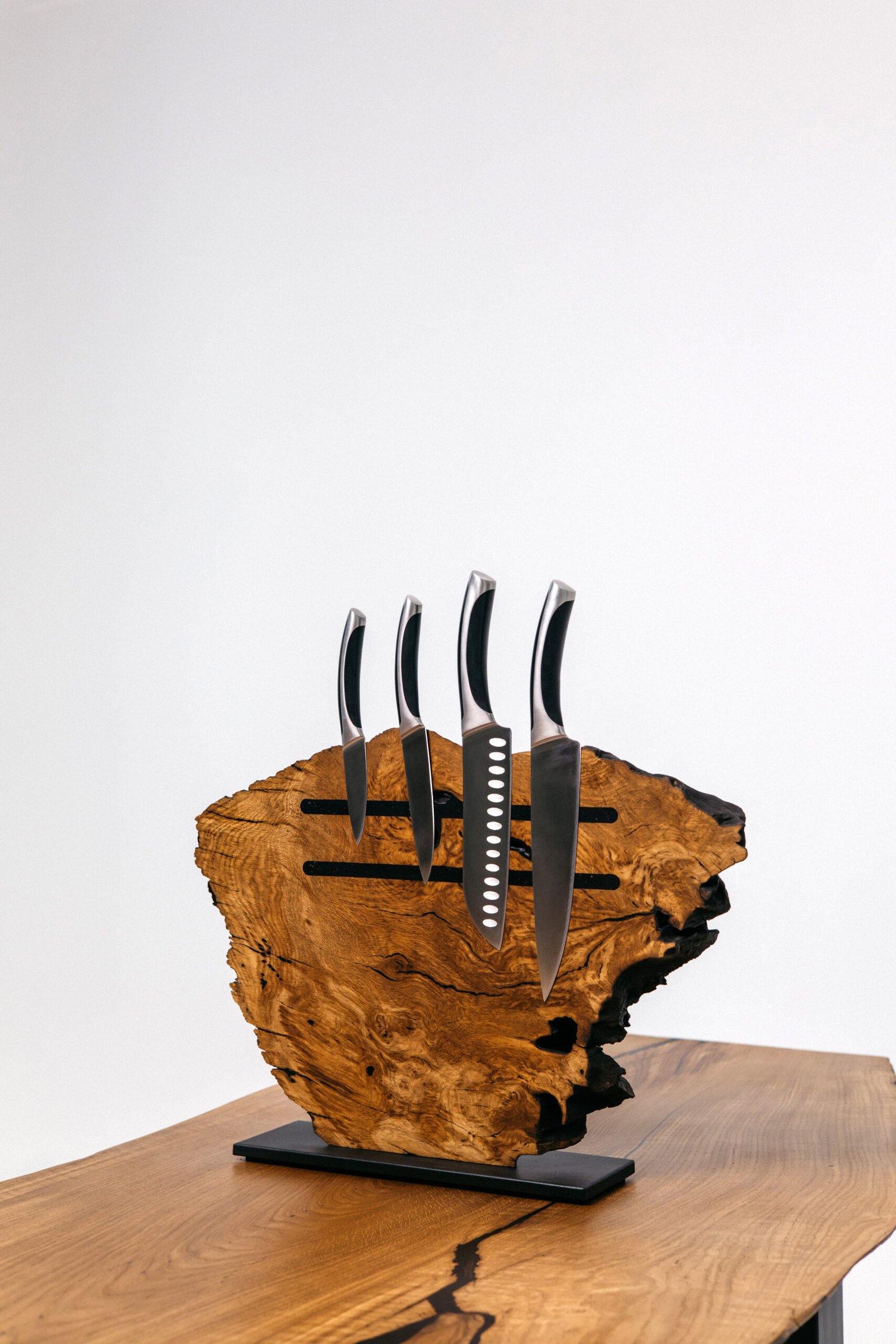 Дерев’яна магнітна підставка для ножів з масиву дерева з природним краєм, на якій вертикально закріплені чотири кухонні ножі з металевими лезами та чорними ручками